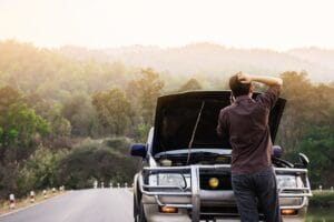 A man next to his car with the hood raised, examining the engine compartment.