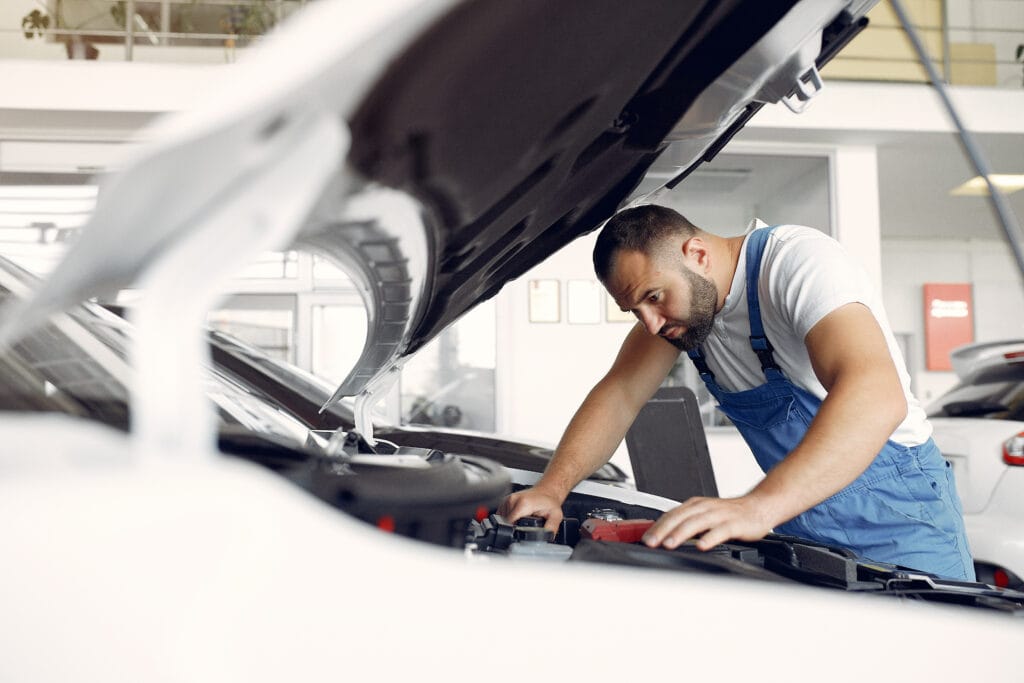 Wrker in a car salon. Expert checks the car. Man in a blue uniform.